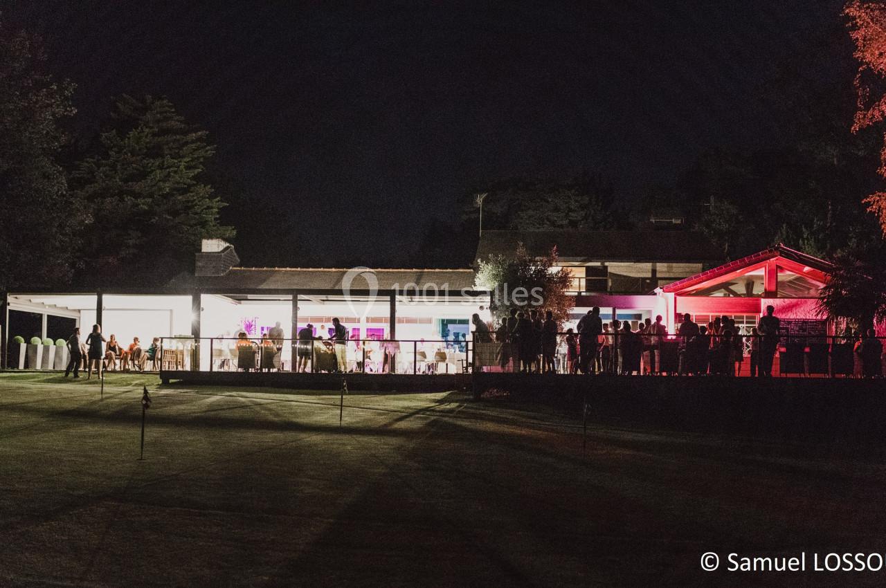 Vue nocturne d'un bâtiment éclairé avec des lumières colorées, entouré de personnes et d'un espace extérieur sombre.