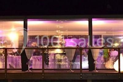 Salle de réception décorée pour un mariage, avec des tables rondes dressées, nappes blanches et arrangements floraux.