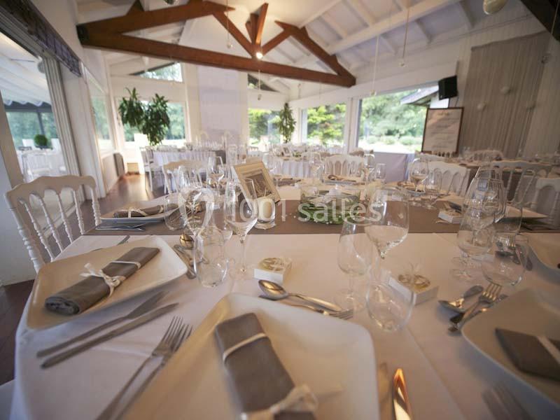 Salle de réception lumineuse avec tables élégamment dressées, nappes blanches, serviettes grises et couverts raffinés.