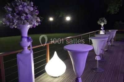 Salle de réception décorée pour un mariage, avec des tables rondes dressées, nappes blanches et arrangements floraux.