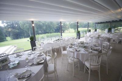 Salle de réception décorée pour un mariage, avec des tables rondes dressées, nappes blanches et arrangements floraux.