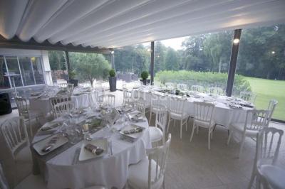 Salle de réception décorée pour un mariage, avec des tables rondes dressées, nappes blanches et arrangements floraux.