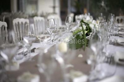 Salle de réception décorée pour un mariage, avec des tables rondes dressées, nappes blanches et arrangements floraux.