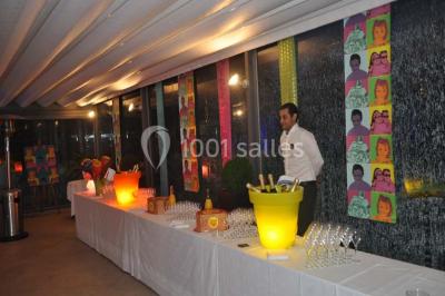 Salle de réception décorée pour un mariage, avec des tables rondes dressées, nappes blanches et arrangements floraux.