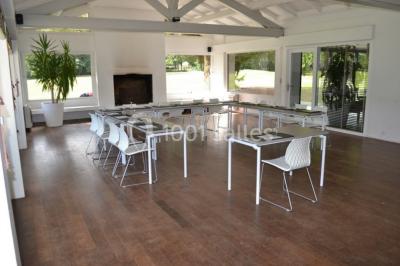 Salle lumineuse avec baies vitrées, tables rondes dressées avec nappes blanches et chaises modernes.