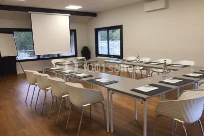 Salle lumineuse avec baies vitrées, tables rondes dressées avec nappes blanches et chaises modernes.