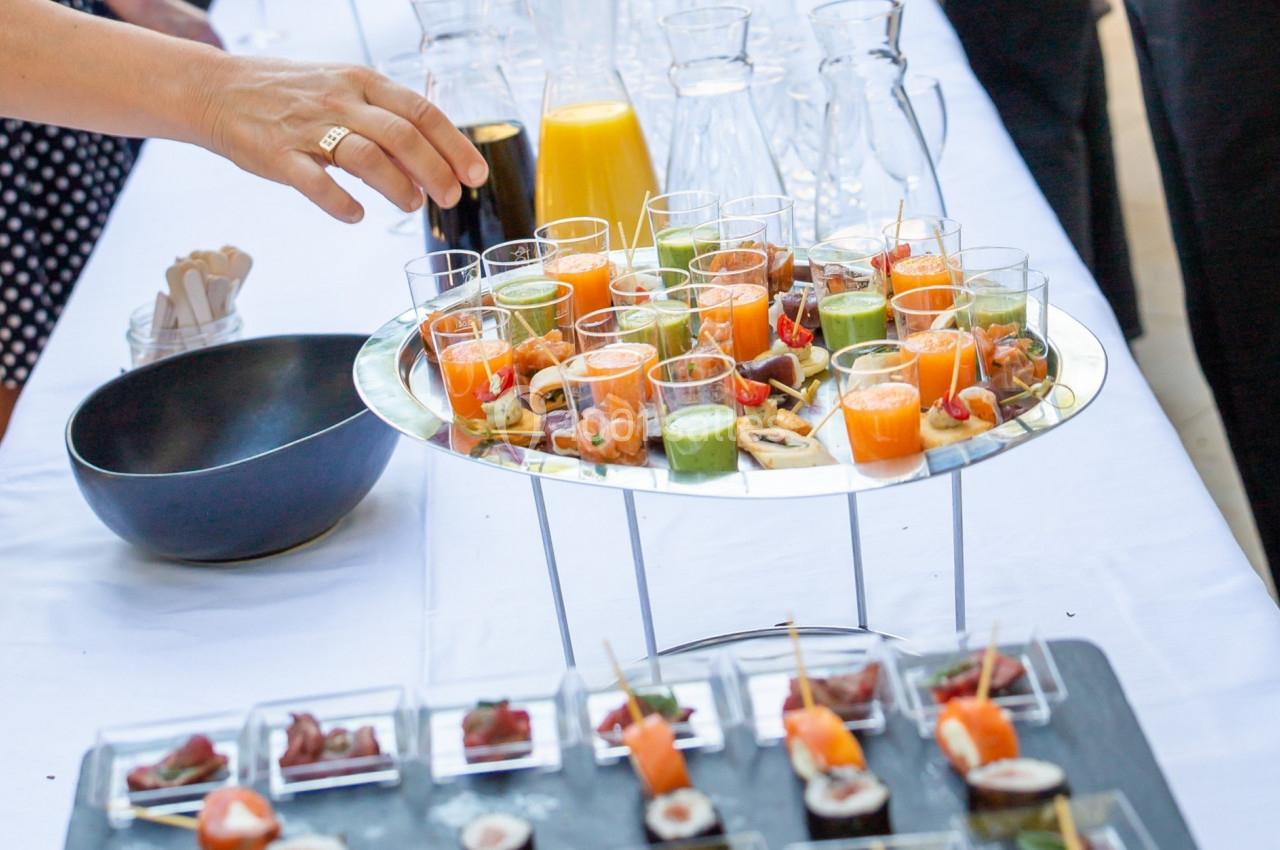 Buffet avec verrines colorées, amuse-bouches variés et boissons, disposé sur une table blanche lors d'un événement.