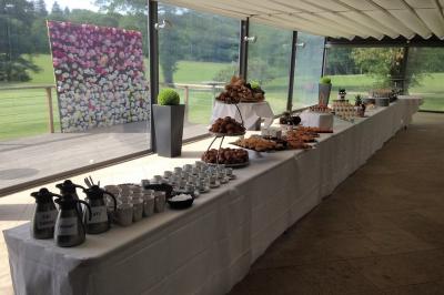 Salle lumineuse avec baies vitrées, tables rondes dressées avec nappes blanches et chaises modernes.