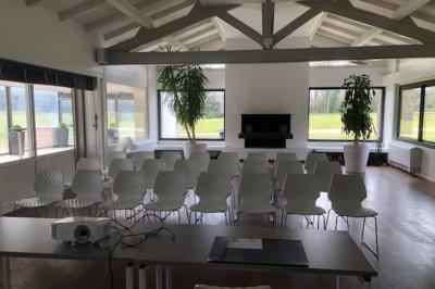 Salle lumineuse avec baies vitrées, tables rondes dressées avec nappes blanches et chaises modernes.