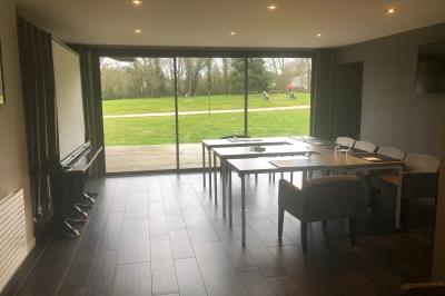 Salle lumineuse avec baies vitrées, tables rondes dressées avec nappes blanches et chaises modernes.