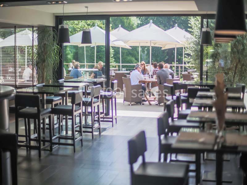 Salle de restaurant lumineuse avec vue sur une terrasse extérieure où des personnes sont assises sous des parasols.