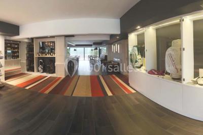 Salle lumineuse avec baies vitrées, tables rondes dressées avec nappes blanches et chaises modernes.