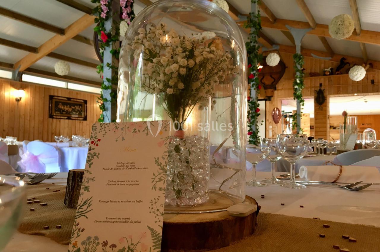 Centre de table avec une cloche en verre contenant des fleurs blanches, posé sur une table de réception décorée.