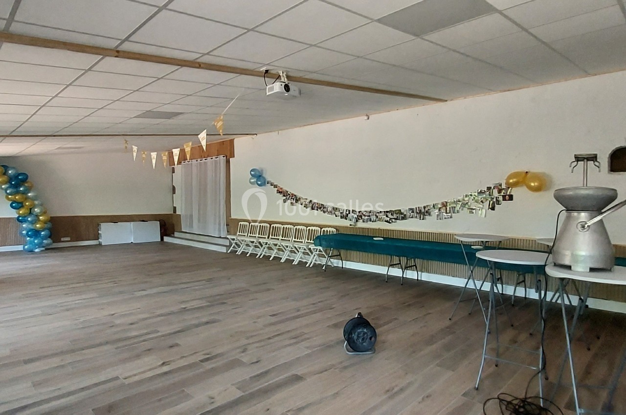 Salle décorée pour un événement avec ballons bleus et jaunes, guirlandes et tables hautes sur un sol en bois.