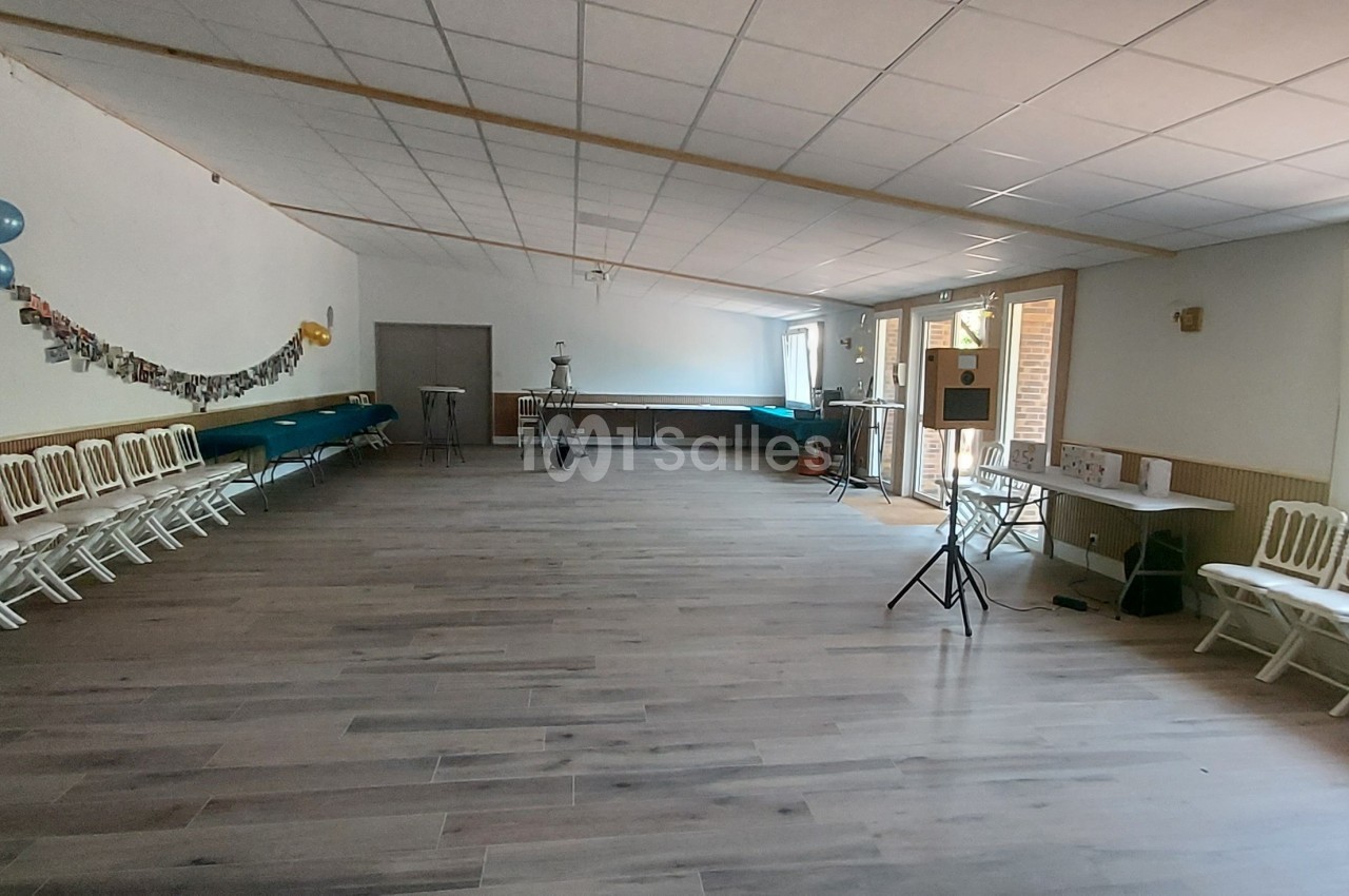 Salle vide avec parquet, chaises alignées le long des murs, décorations murales et lumière naturelle entrant par une porte…