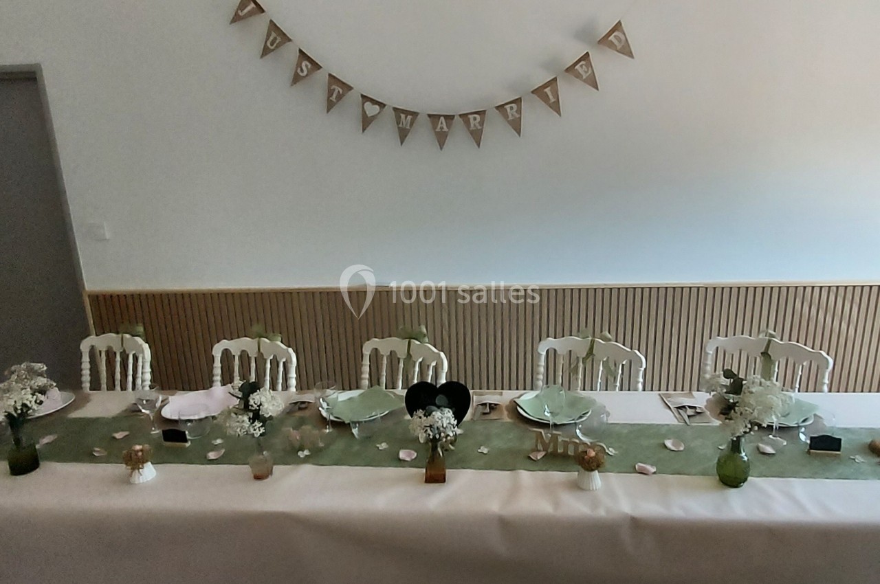 Table décorée pour un événement, avec nappes blanches, chemins de table verts, vaisselle et ornements floraux.