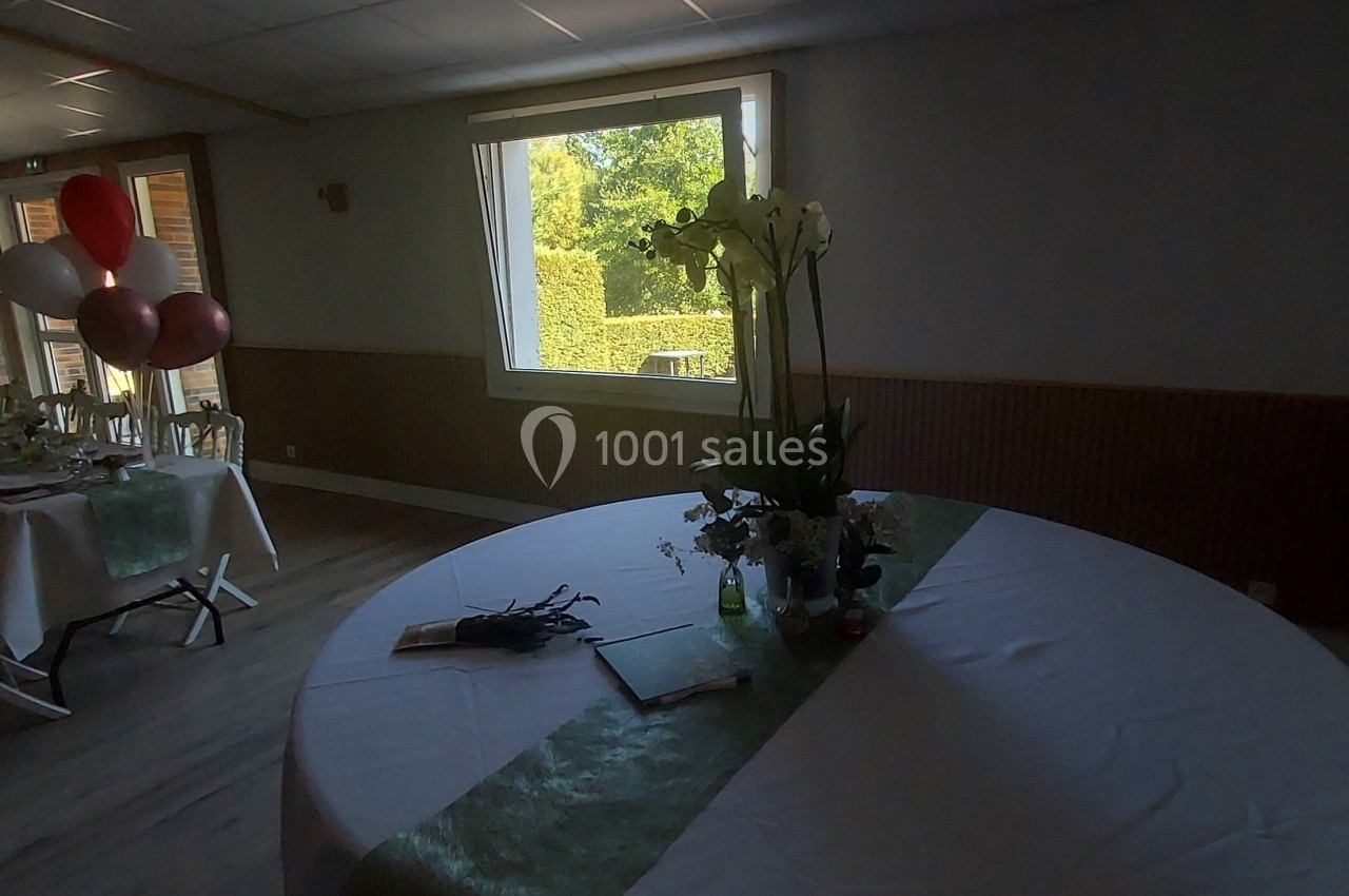 Salle de réception avec une table ronde décorée, des ballons et une grande table dressée en arrière-plan.