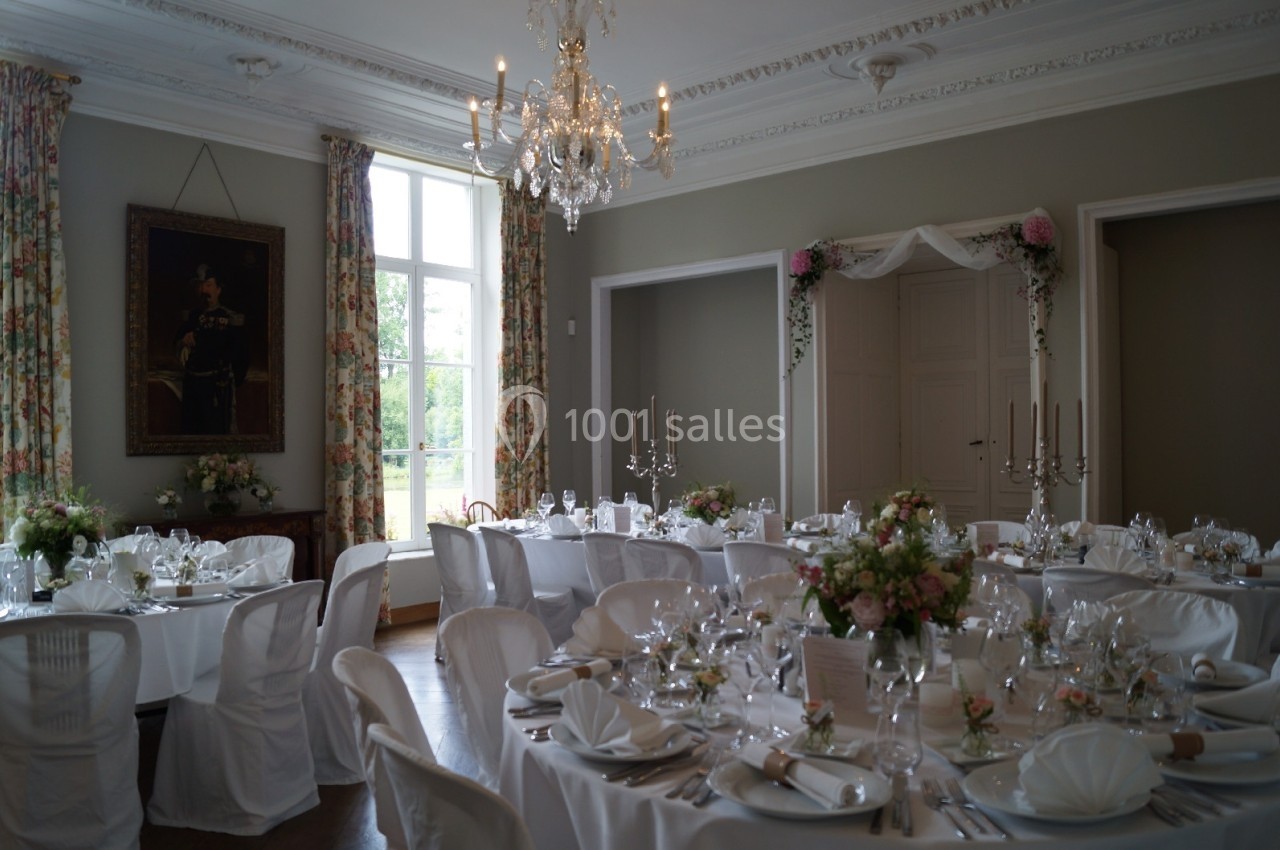 Salle élégante décorée pour un mariage, avec tables dressées, nappes blanches, chandeliers et fleurs.
