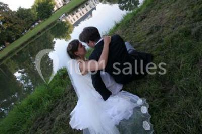 Une femme en robe de mariée défile sur un tapis rouge devant un public dans une salle éclairée par des lustres.