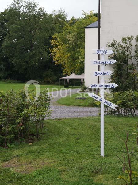 Panneau directionnel en bois dans un jardin, indiquant des lieux tels que ’cérémonie’ et ’livre d'or’.