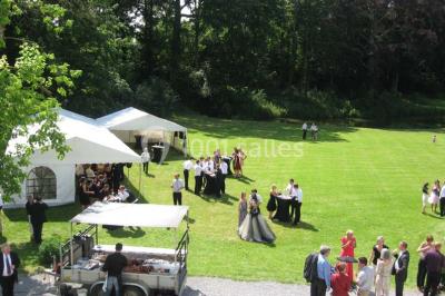 Une femme en robe de mariée défile sur un tapis rouge devant un public dans une salle éclairée par des lustres.