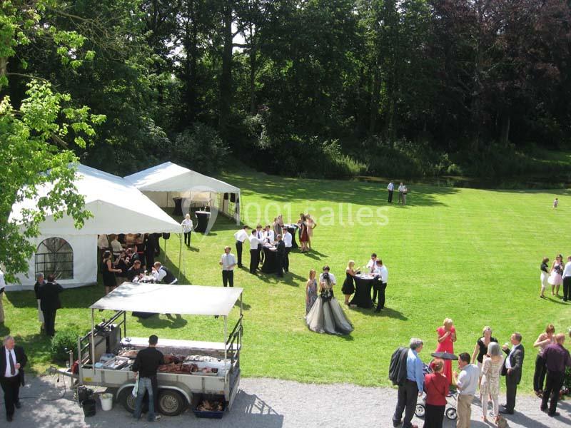 Groupe de personnes rassemblées dans un jardin pour un événement, avec tentes blanches et stand de restauration.