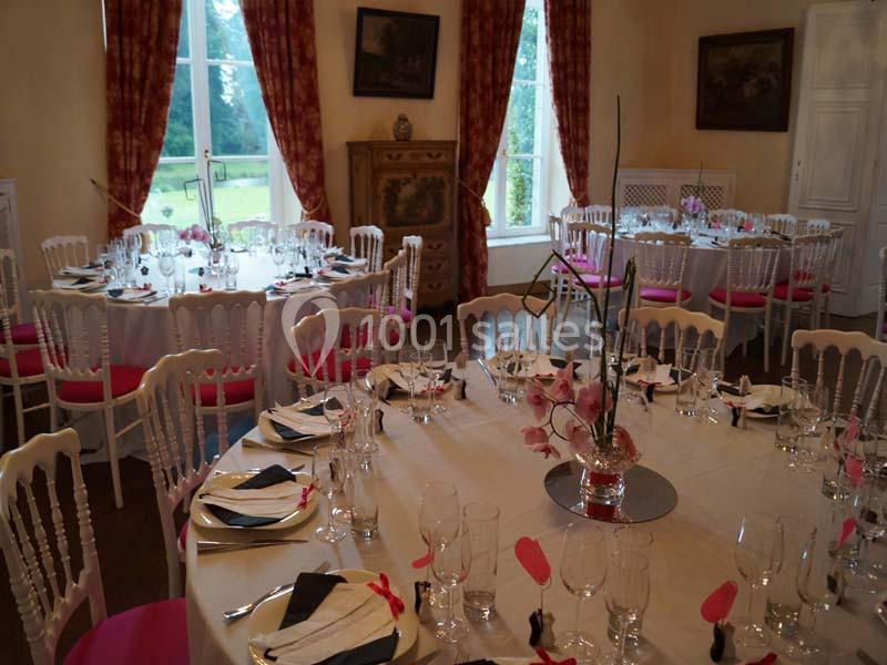 Salle de réception élégante avec tables rondes dressées, nappes blanches, chaises décorées et centre de table floral.