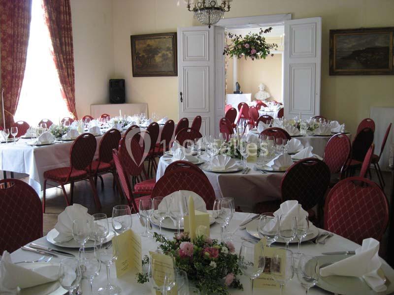 Salle de réception élégante avec tables dressées, nappes blanches, chaises rouges et décorations florales.