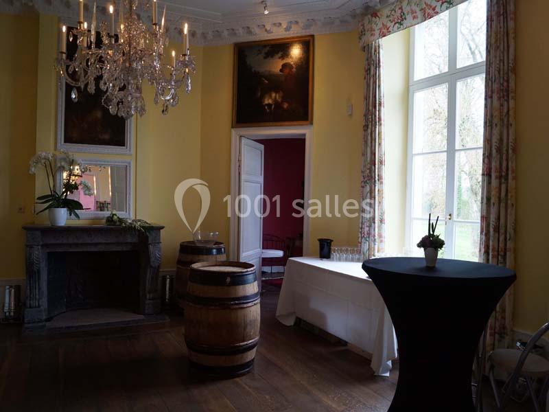 Salle élégante avec murs jaunes, cheminée, lustre, tonneaux en bois, table dressée et grande fenêtre donnant sur l'extérieur.