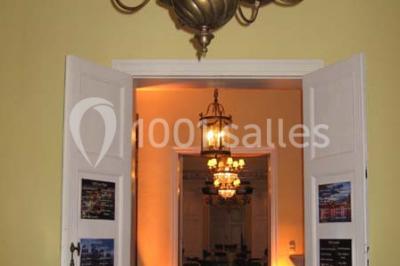 Une femme en robe de mariée défile sur un tapis rouge devant un public dans une salle éclairée par des lustres.