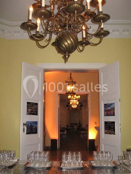 Vue d'une salle élégante avec des lustres, des portes ouvertes et une table dressée avec des verres en premier plan.