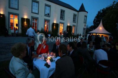 Une femme en robe de mariée défile sur un tapis rouge devant un public dans une salle éclairée par des lustres.