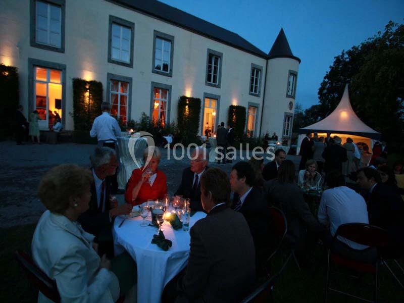 Groupe de personnes dînant en soirée à l'extérieur, devant un bâtiment éclairé et une tente blanche.