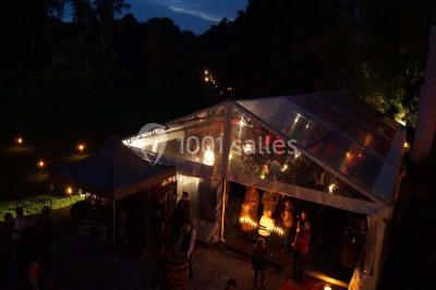 Une femme en robe de mariée défile sur un tapis rouge devant un public dans une salle éclairée par des lustres.