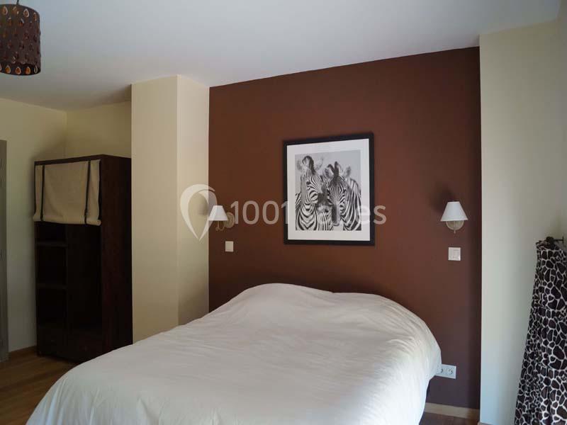 Chambre avec un lit double, mur brun décoré d'un tableau de zèbres, et armoire en bois sombre.