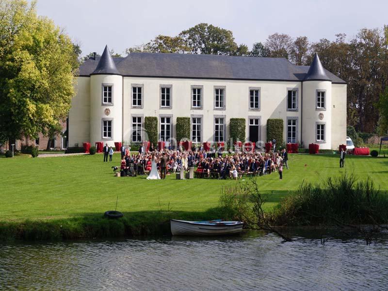 Groupe de personnes rassemblées devant un château avec pelouse, arbres et un plan d'eau au premier plan.