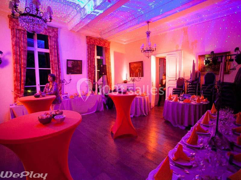Salle décorée pour un événement, avec tables nappées, éclairage coloré et ambiance festive.