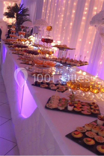 Buffet de desserts variés disposés sur une longue table décorée de lumières et nappes blanches dans une salle festive.