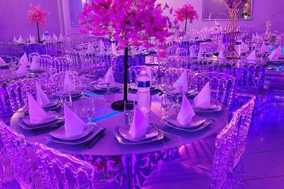 Salle de réception décorée avec des lumières roses et un éclairage scintillant, tables dressées et plafond drapé.