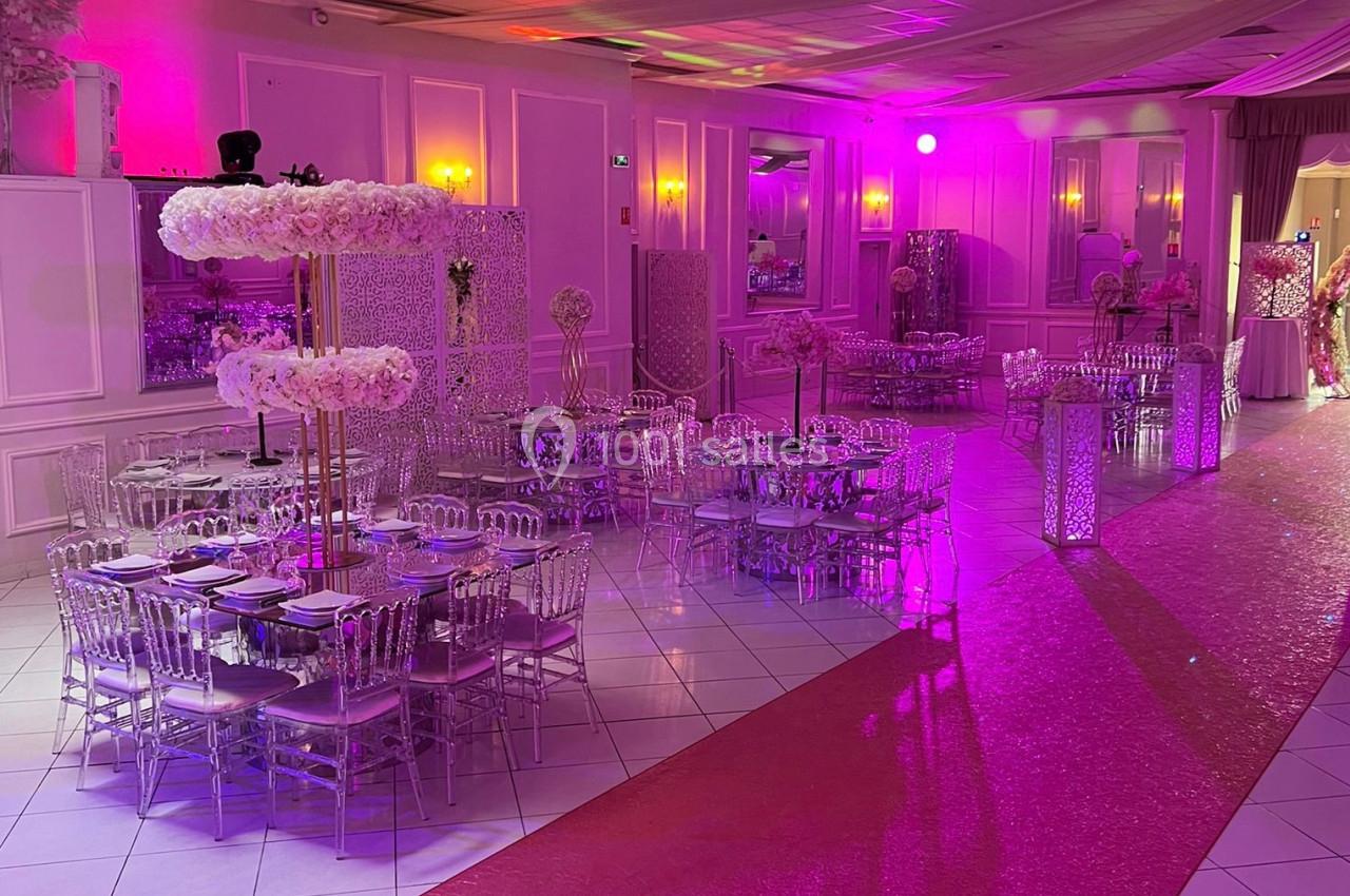 Salle de réception décorée avec des tables rondes, chaises transparentes et éclairage rose.