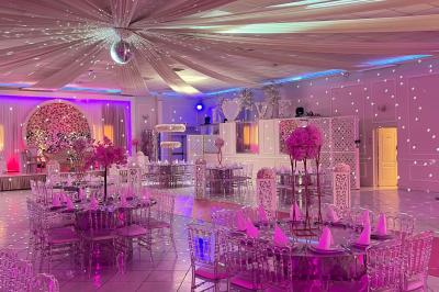 Salle de réception décorée avec des lumières roses et un éclairage scintillant, tables dressées et plafond drapé.