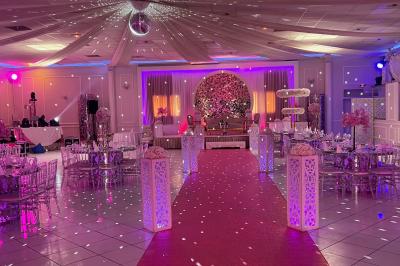 Salle de réception décorée avec des lumières roses et un éclairage scintillant, tables dressées et plafond drapé.