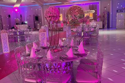 Salle de réception décorée avec des lumières roses et un éclairage scintillant, tables dressées et plafond drapé.