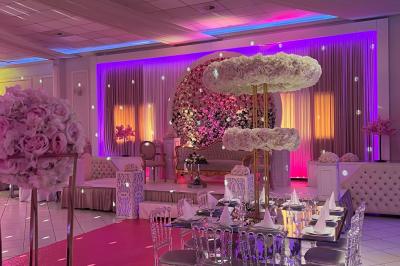 Salle de réception décorée avec des lumières roses et un éclairage scintillant, tables dressées et plafond drapé.