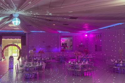 Salle de réception décorée avec des lumières roses et un éclairage scintillant, tables dressées et plafond drapé.