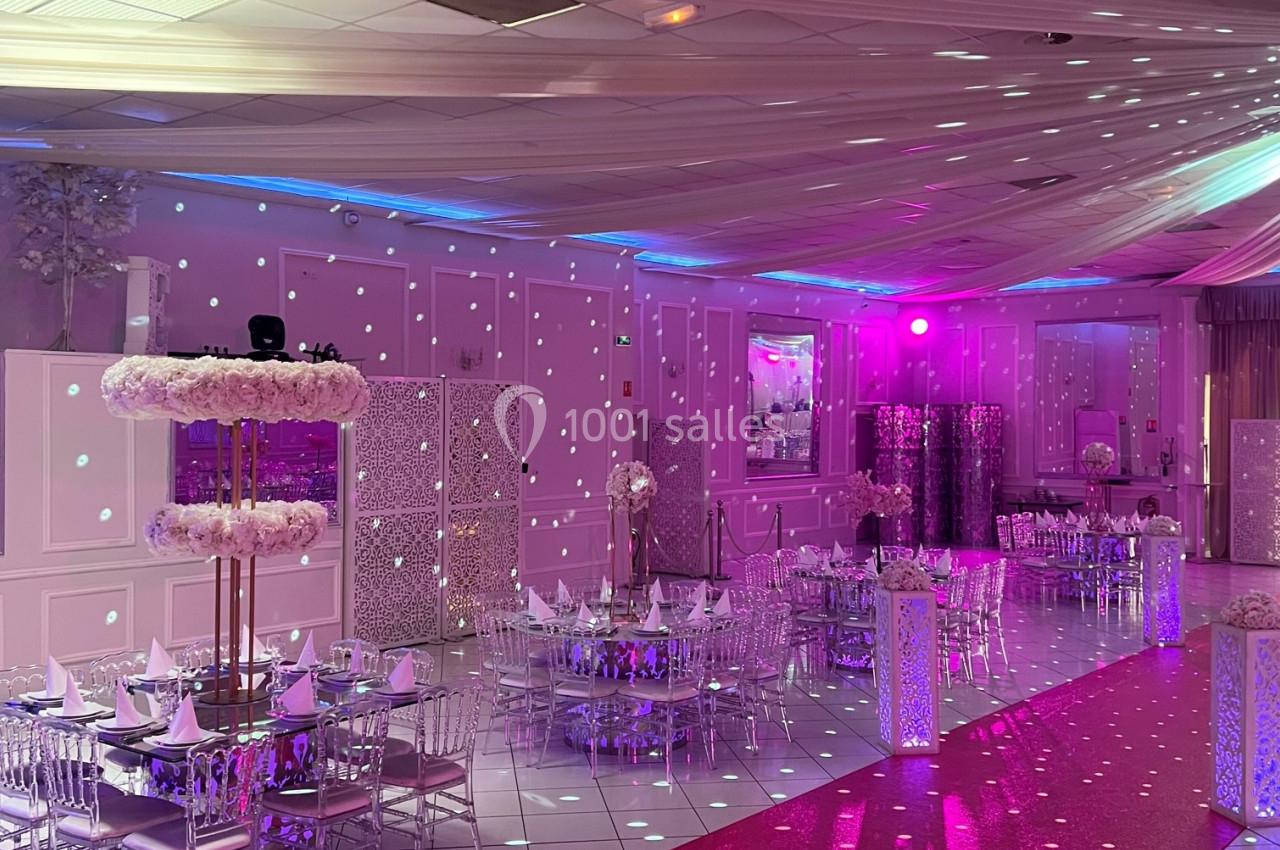 Salle de réception décorée avec des tables dressées, un tapis rouge et un éclairage rose et scintillant.