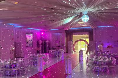 Salle de réception décorée avec des lumières roses et un éclairage scintillant, tables dressées et plafond drapé.