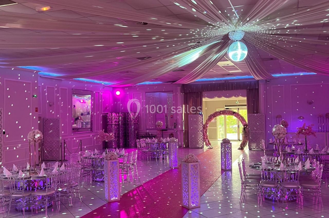 Salle de réception décorée avec des tables dressées, un tapis rouge et une boule disco projetant des lumières.