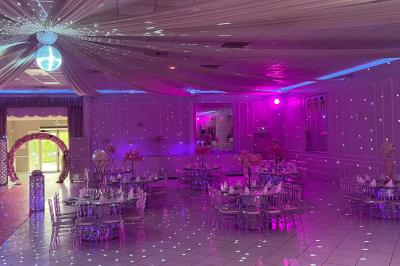 Salle de réception décorée avec des lumières roses et un éclairage scintillant, tables dressées et plafond drapé.