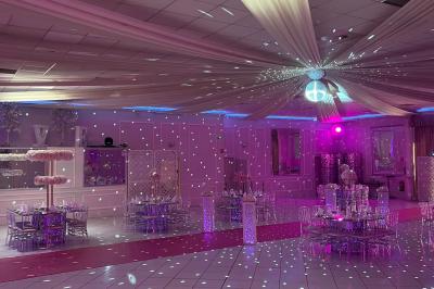 Salle de réception décorée avec des lumières roses et un éclairage scintillant, tables dressées et plafond drapé.